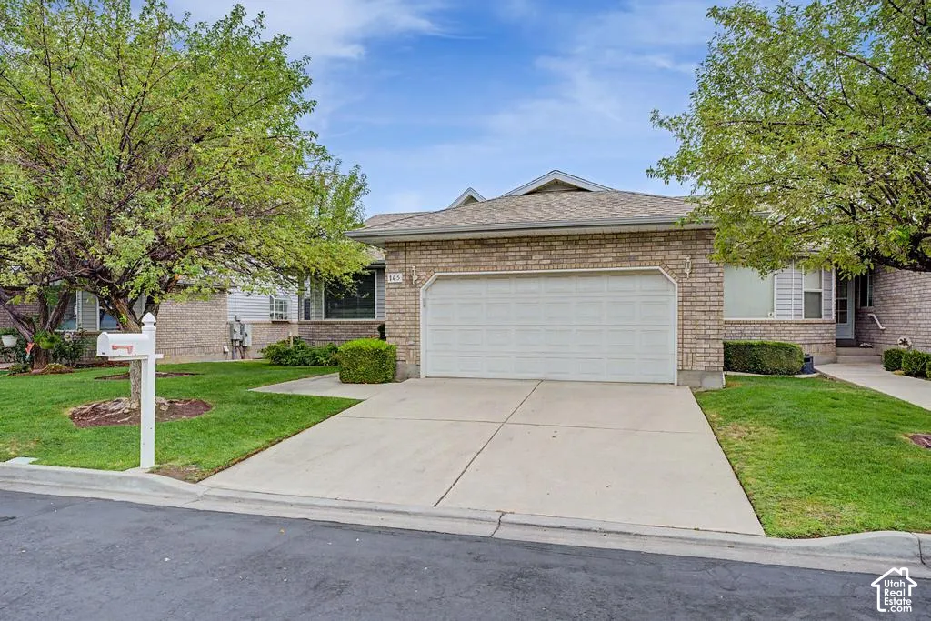 Brick exterior, attached garage, concrete driveway, and front yard with mature trees.