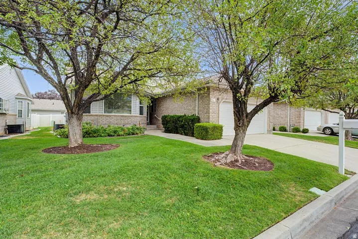 Brick exterior with white garage doors, mature front yard trees, and a concrete driveway
