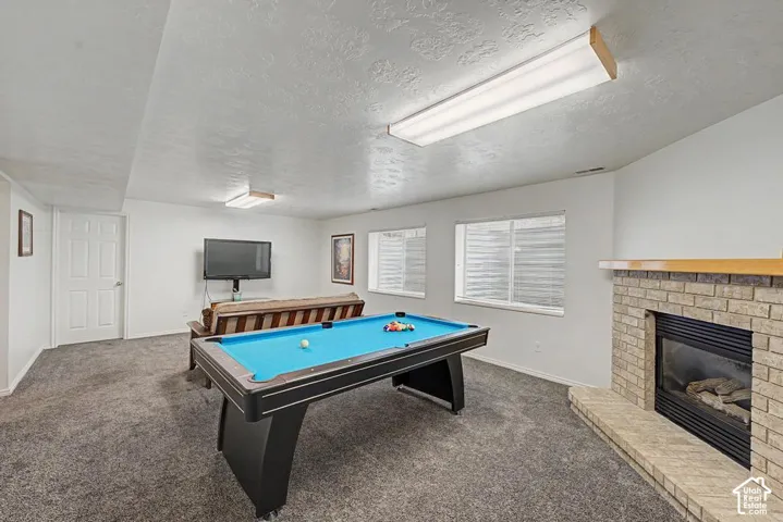 Spacious lower-level family room featuring carpeted flooring and a stone-clad fireplace with a wood mantle.