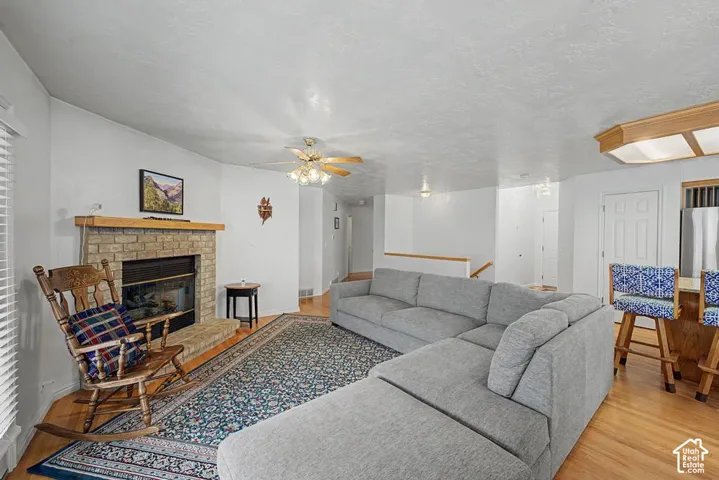 Brick-surround fireplace with a wood mantle, hardwood flooring, and a ceiling fan with integrated lighting