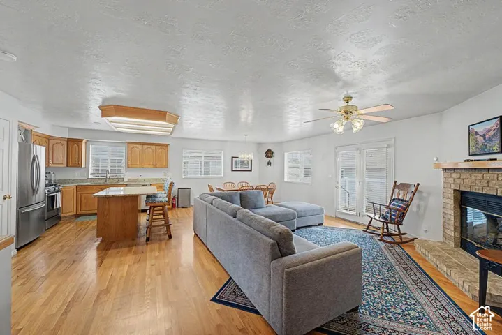 Open-concept living space featuring hardwood floors, a kitchen island with seating, a fireplace with a stone surround, and French doors