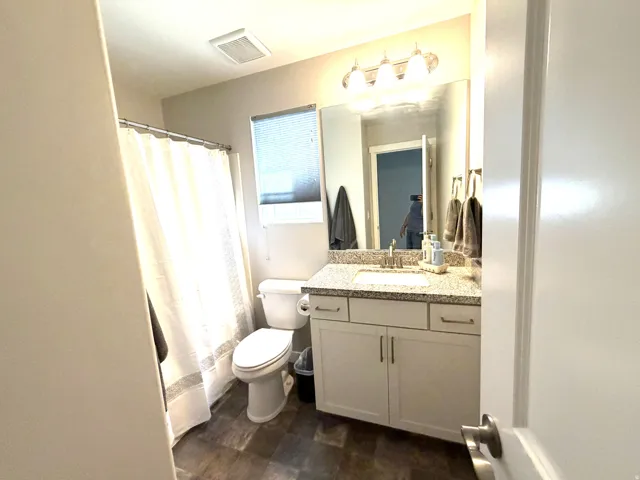 Bathroom featuring a vanity with granite-style countertop, undermount sink, and wood-finish flooring