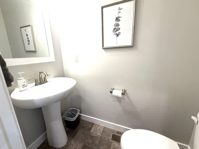 Pedestal sink with a two-handle faucet, wall-mounted mirror with a white frame, and wood-finish flooring