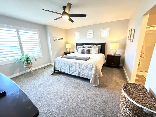 Window with plantation shutters, overhead ceiling fan, dark wood-finish nightstands, and wall-to-wall carpeting