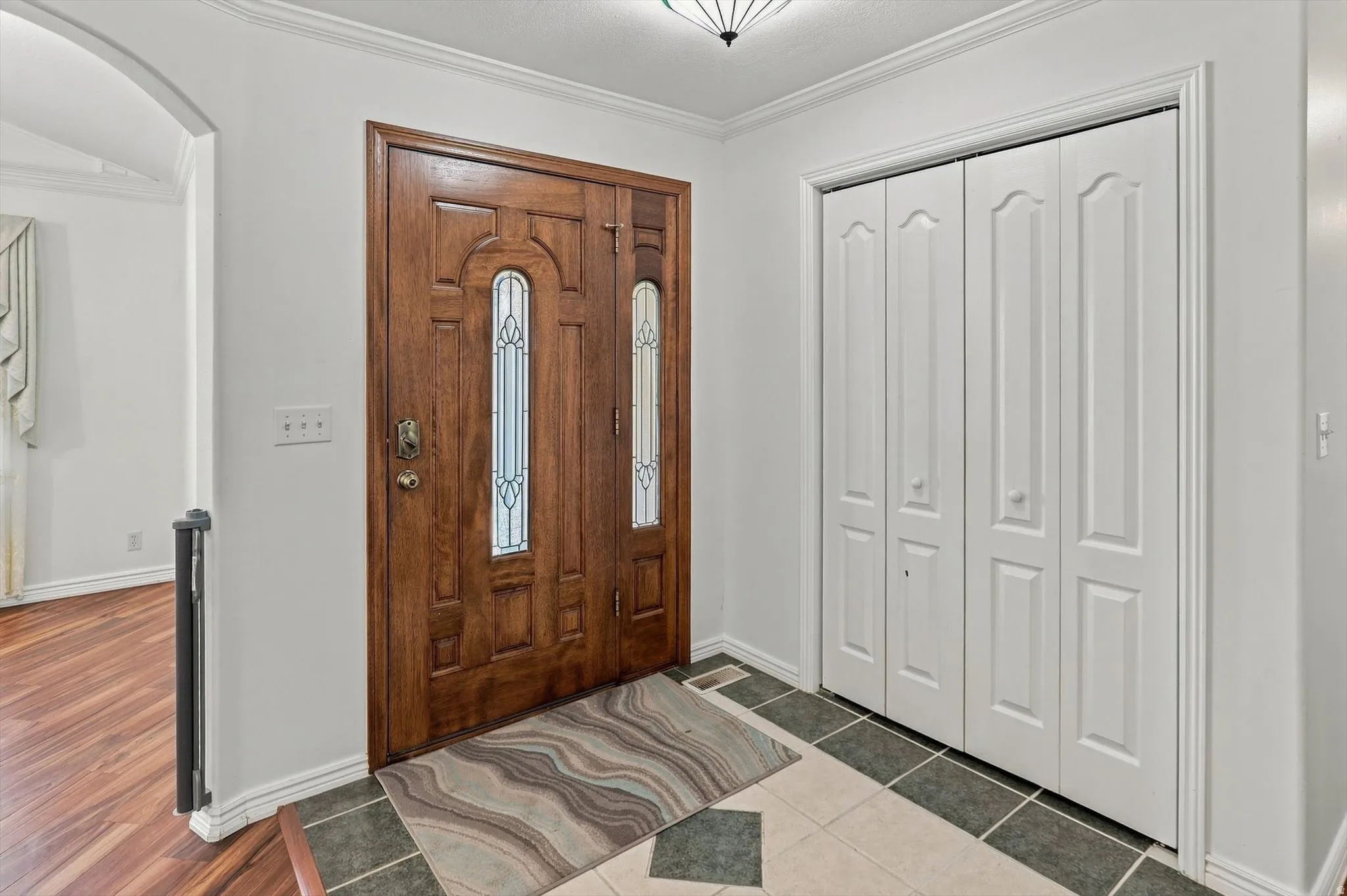 Hardwood entry door with decorative glass inserts, crown molding, and bifold closet doors