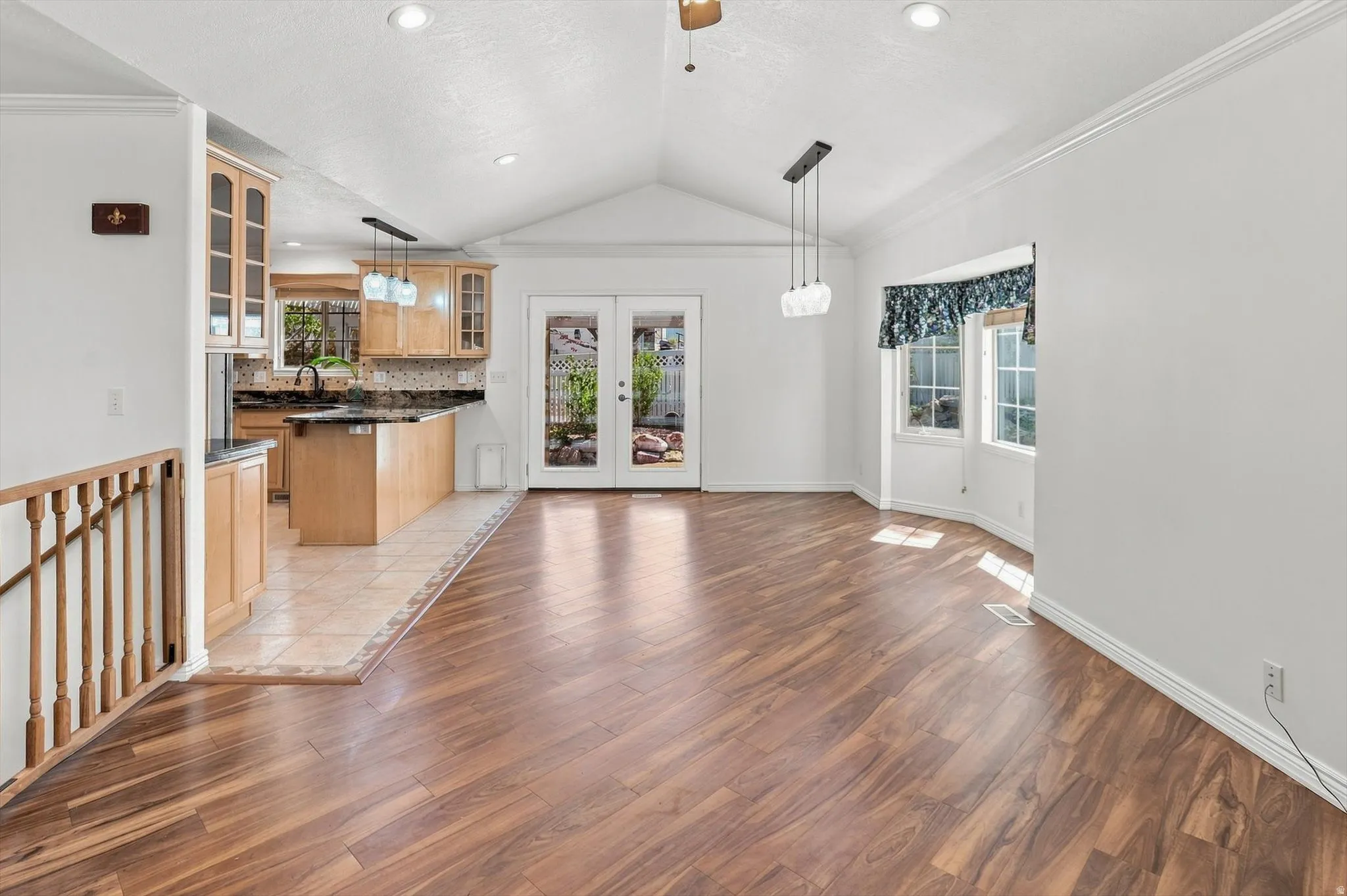 Vaulted ceiling with a ceiling fan, wood-finish flooring, and a bay window