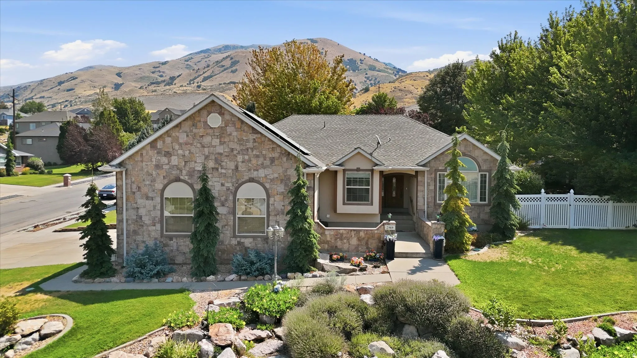 Stone facade, arched windows, covered entry, and manicured landscaping with a vibrant green lawn