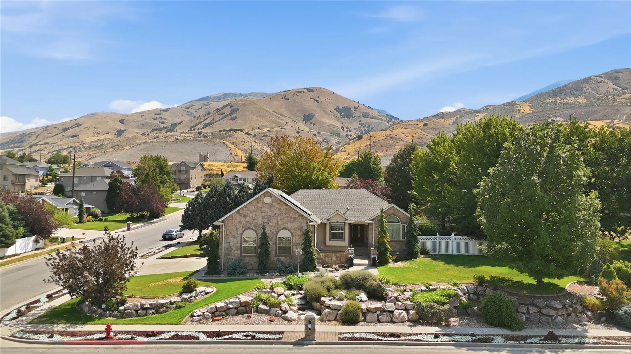 Stone exterior, arched windows, gabled roofline, mature landscaping, and an expansive front yard