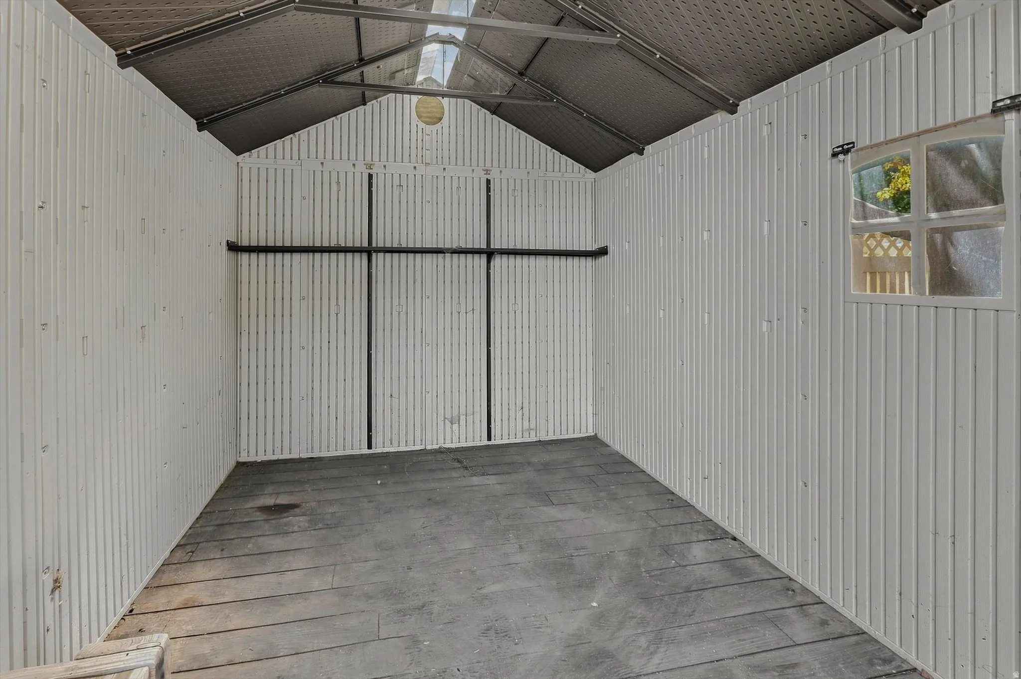 Corrugated metal walls, exposed rafter ceiling, wood-finish flooring, and a single window