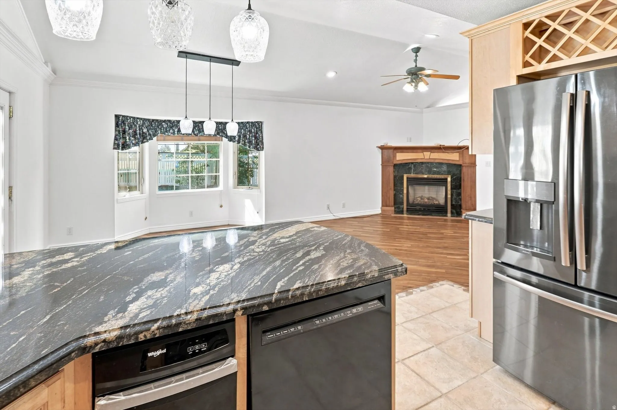Stainless steel appliances, built-in wine rack, kitchen island with built-in dishwasher, wood-finish flooring, and fireplace with wood mantel