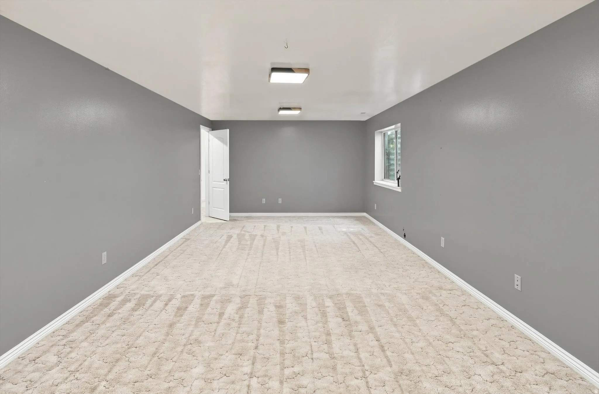 Spacious room featuring neutral carpeting, a white interior door, and a single window