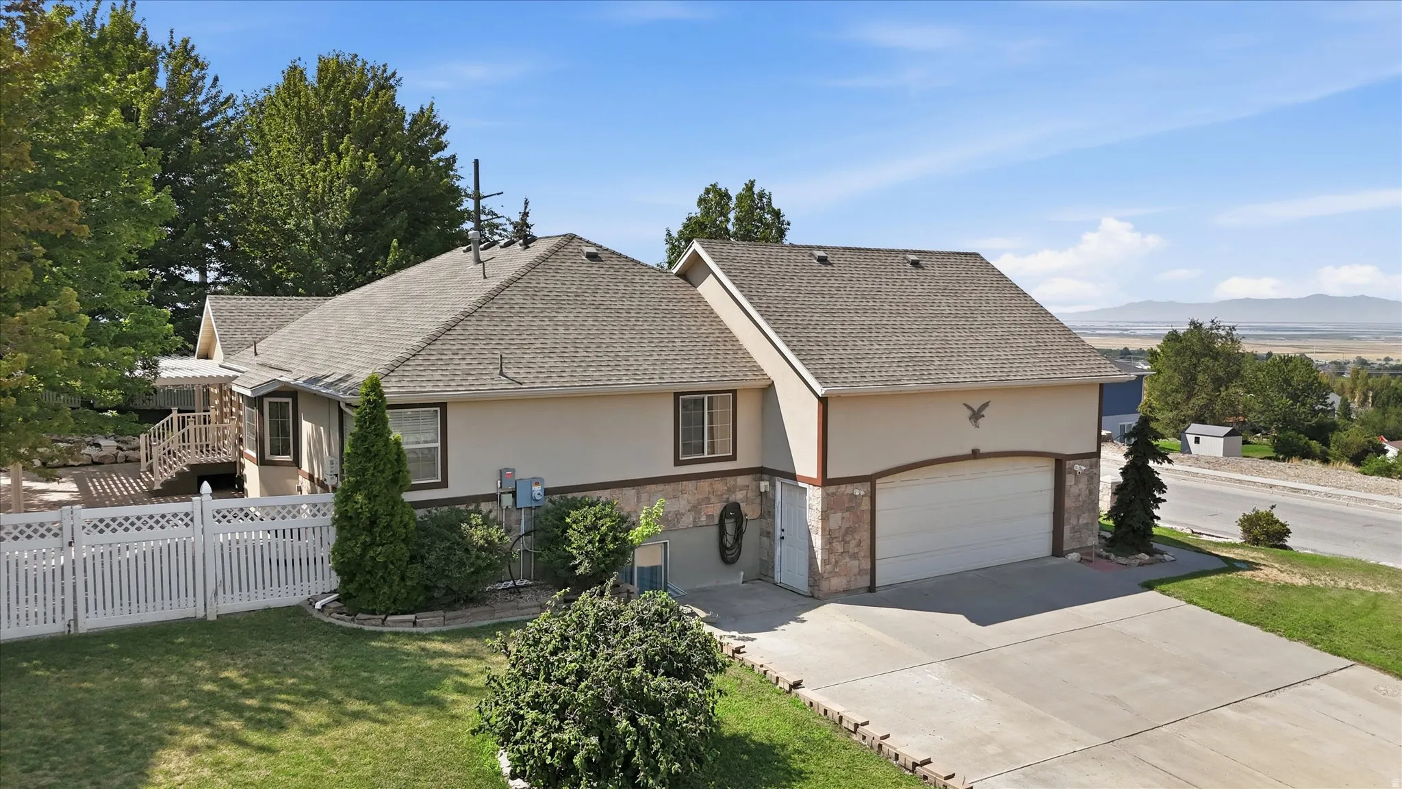 Exterior with a two-car garage, stone accent siding, asphalt shingle roof, and a white picket fence