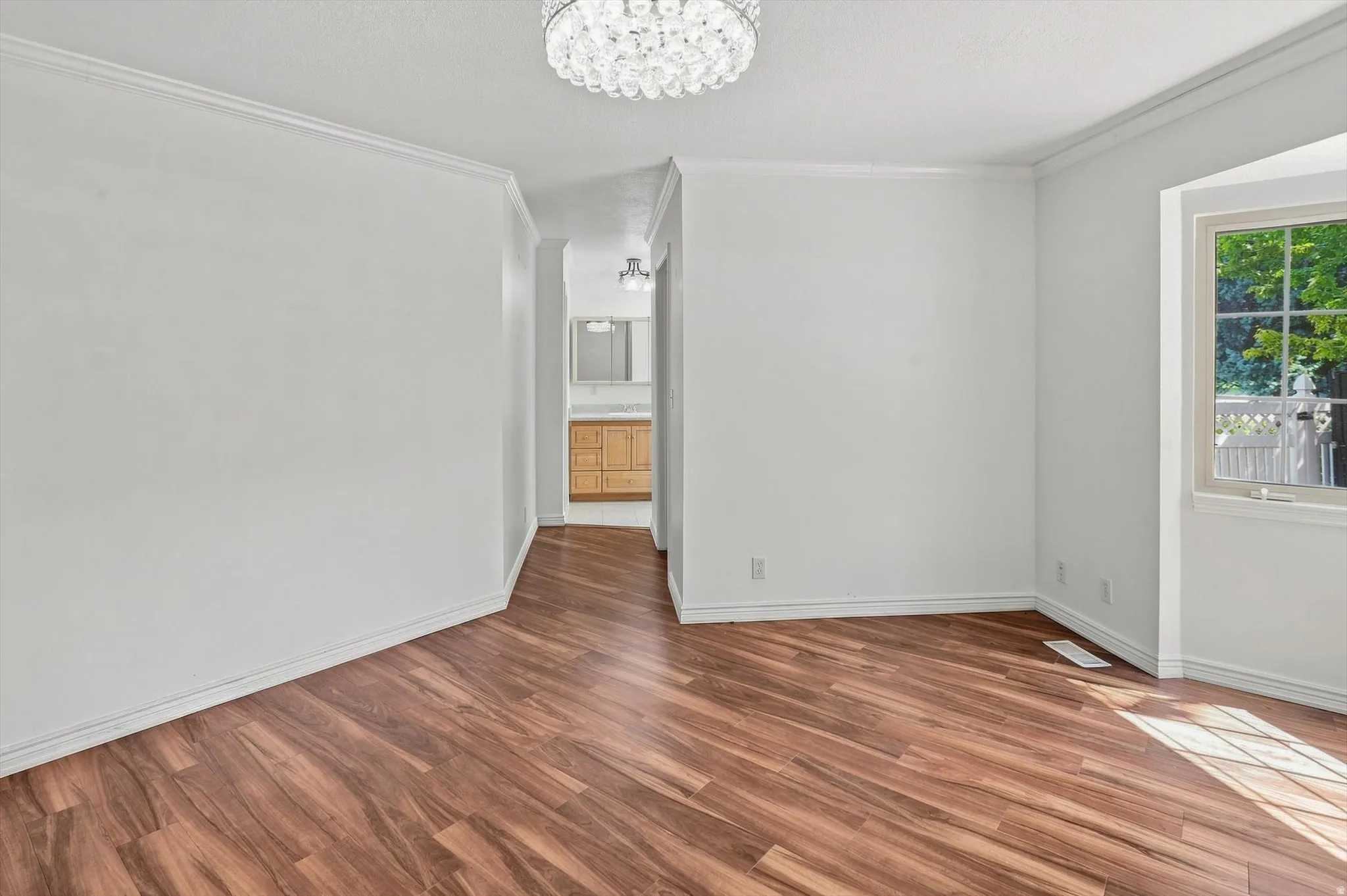 Wood-finish flooring throughout, bright white walls, crown molding, and a multi-pane window