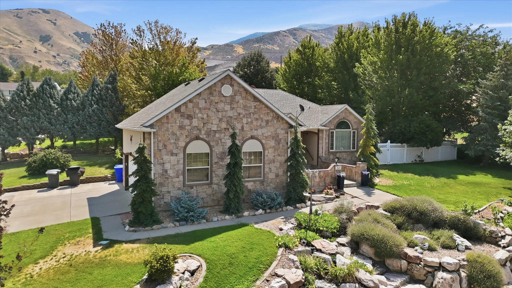 Stone veneer exterior with arched windows, mature landscaping, and a mountain backdrop
