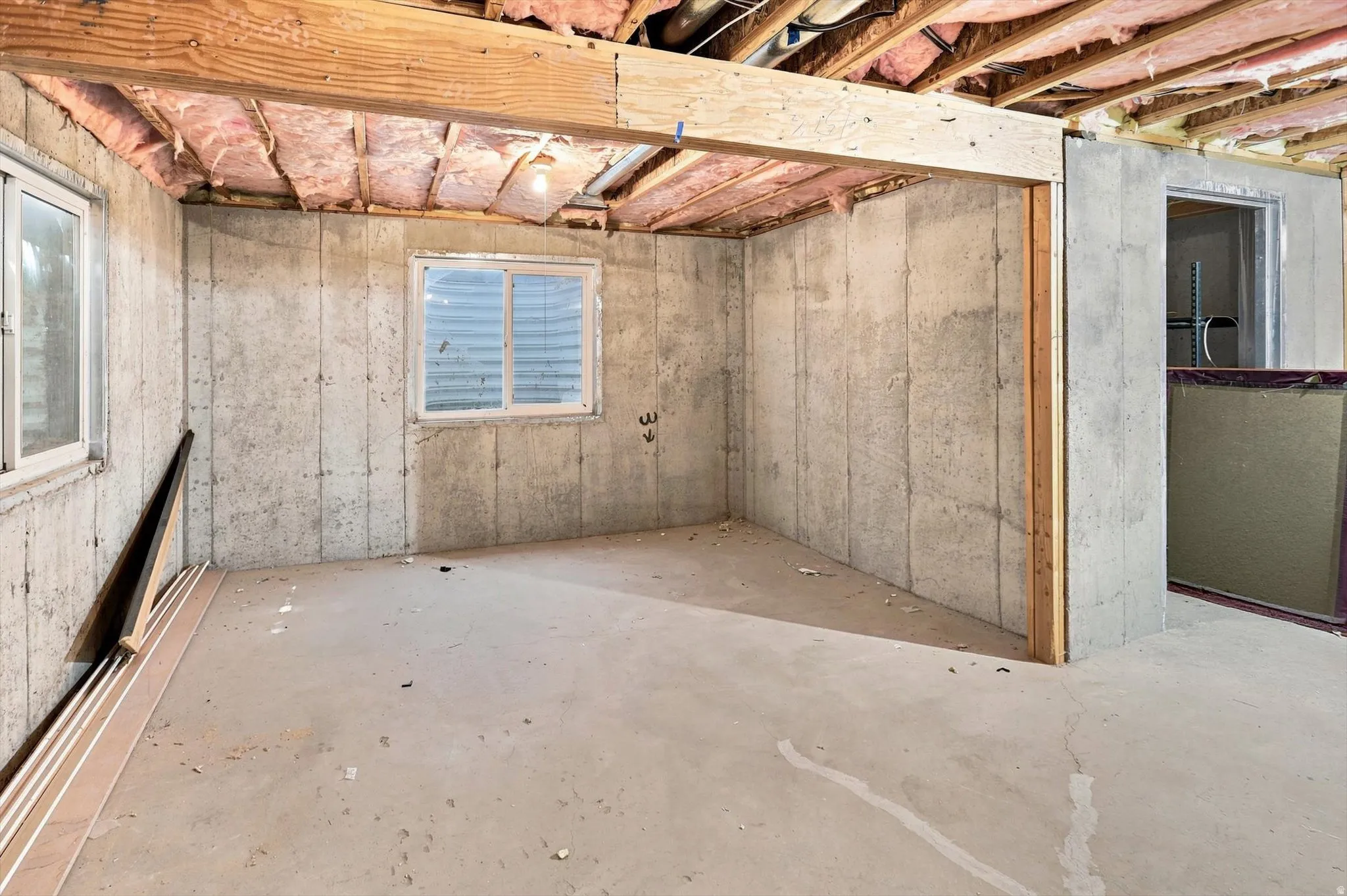 Exposed wood beams, concrete foundation walls, two windows, and concrete flooring