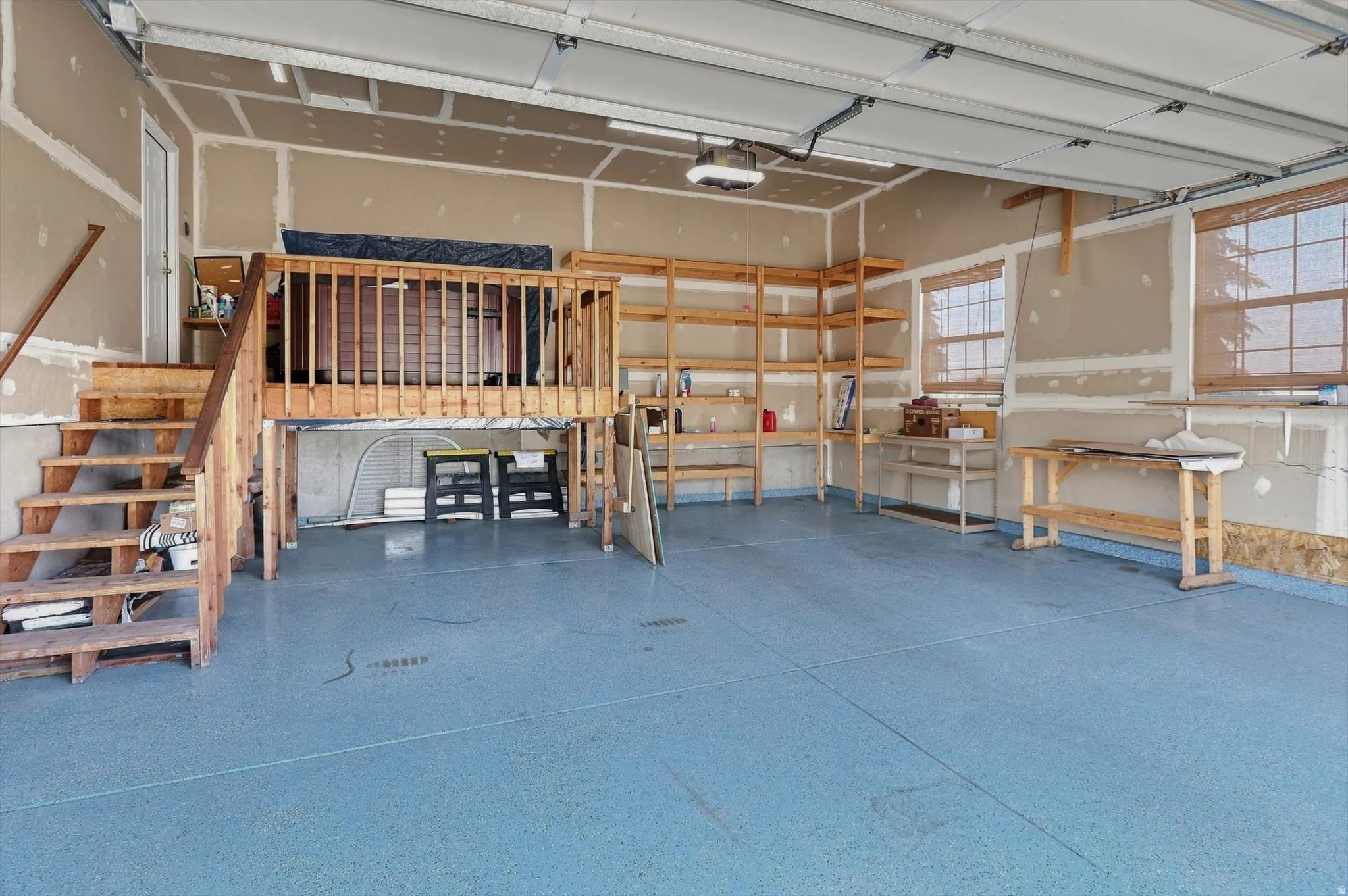 Epoxy-coated flooring, built-in shelving, elevated storage platform, exposed wooden staircase, and multiple windows