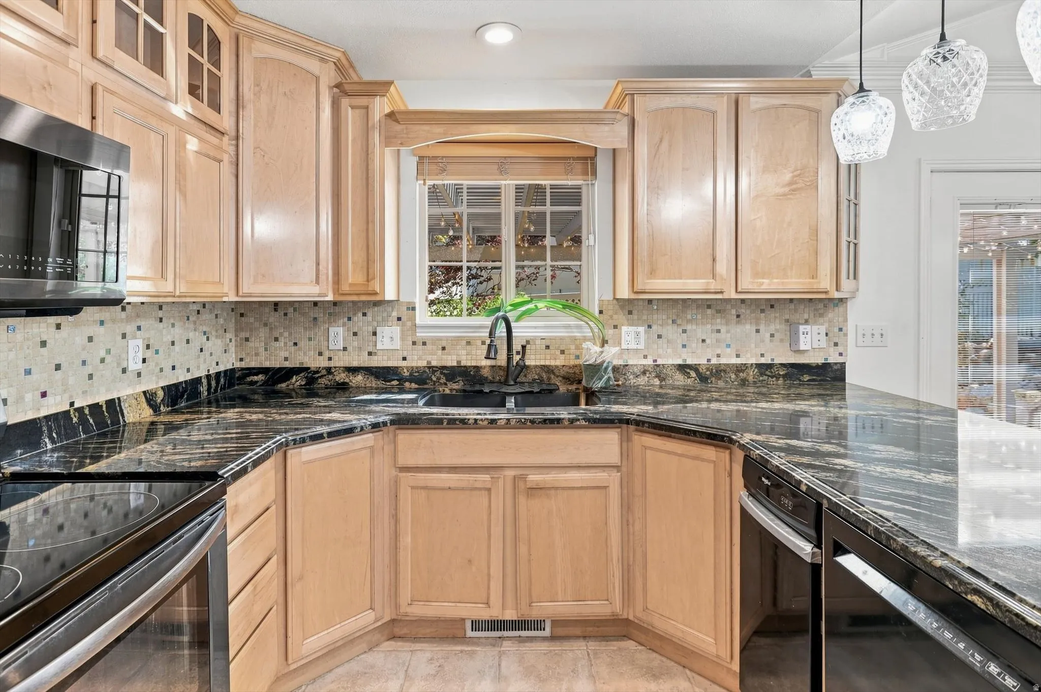 U-shaped kitchen featuring light wood cabinetry, dark polished countertops, mosaic tile backsplash, and stainless steel appliances