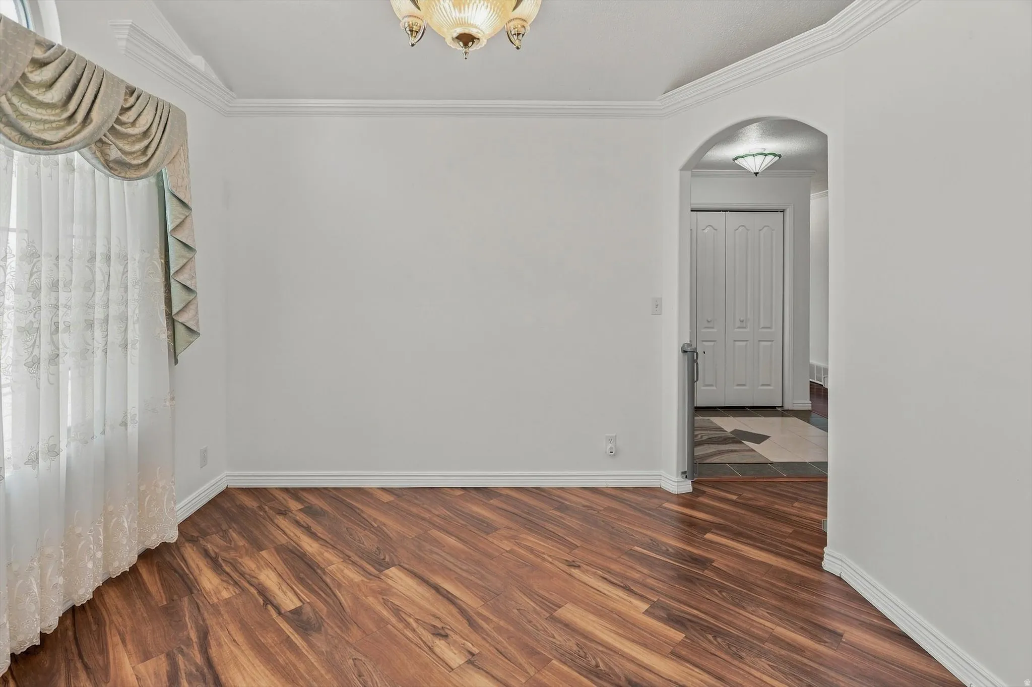 Wood-finish flooring, crown molding, and an arched entryway