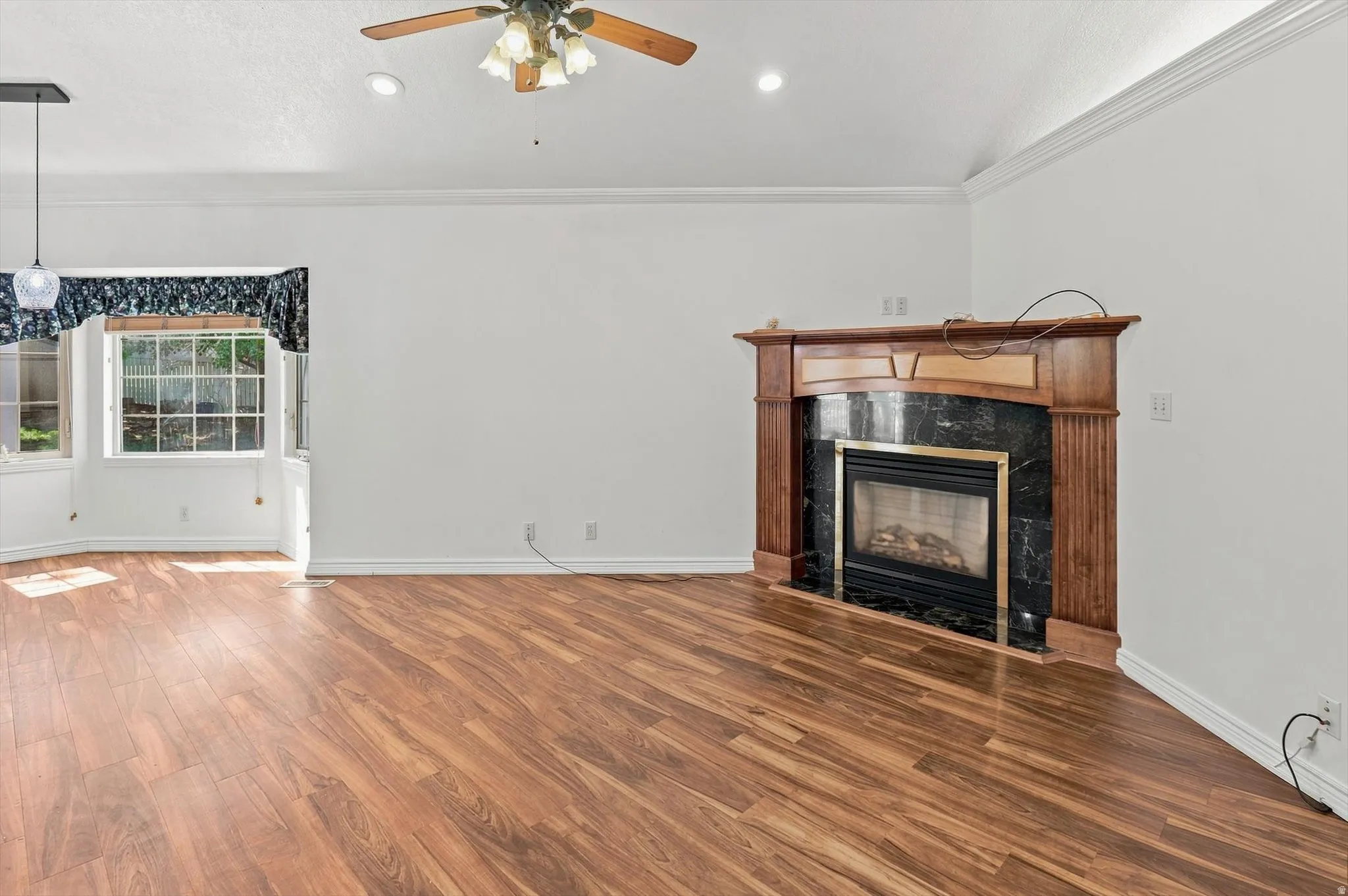 Wood-finish flooring, a ceiling fan with integrated lighting, recessed lighting, and a fireplace with a dark stone surround and wood mantle