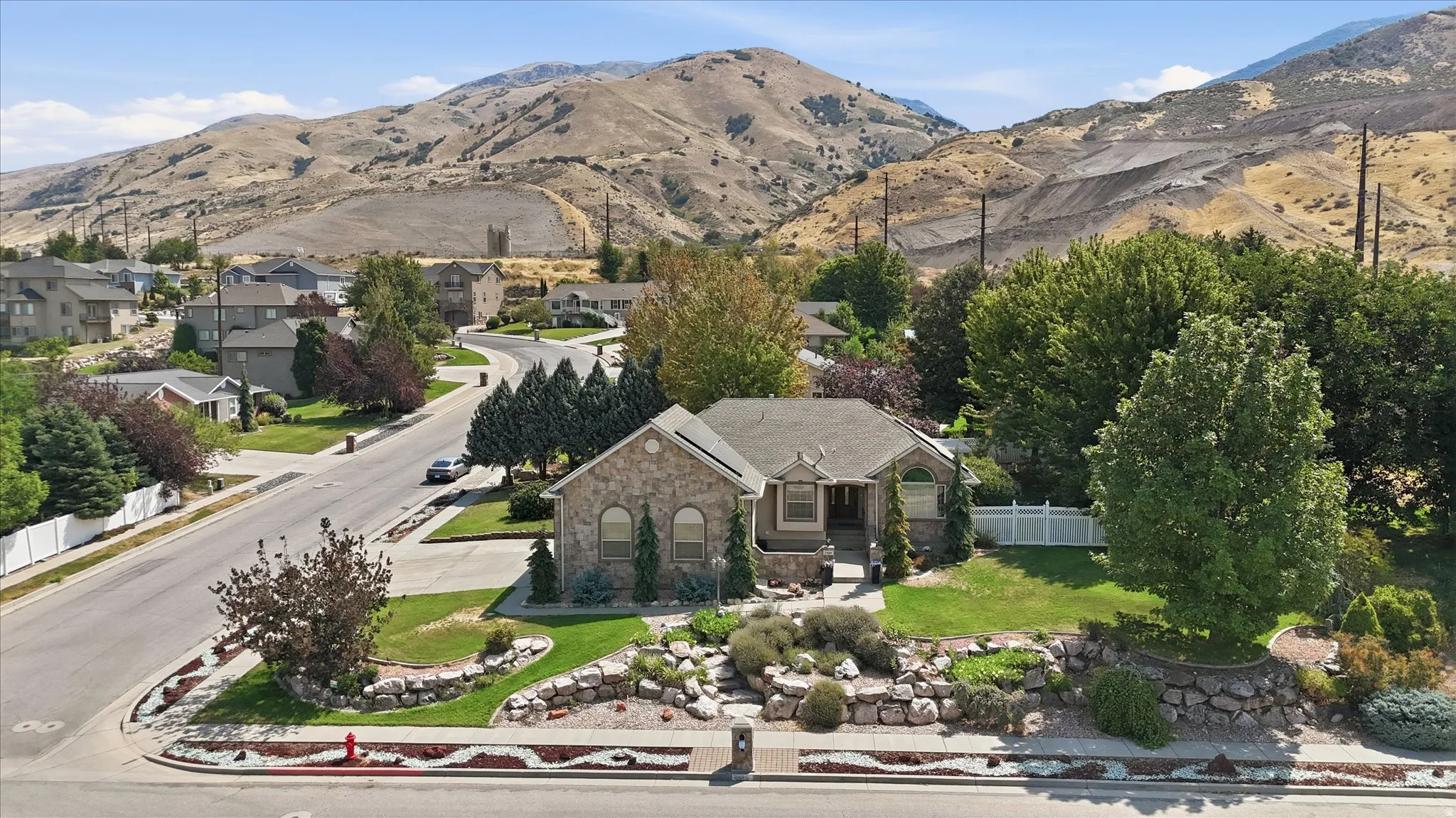 Stone exterior residence situated on manicured grounds featuring mature landscaping, established trees, and curved driveway entry