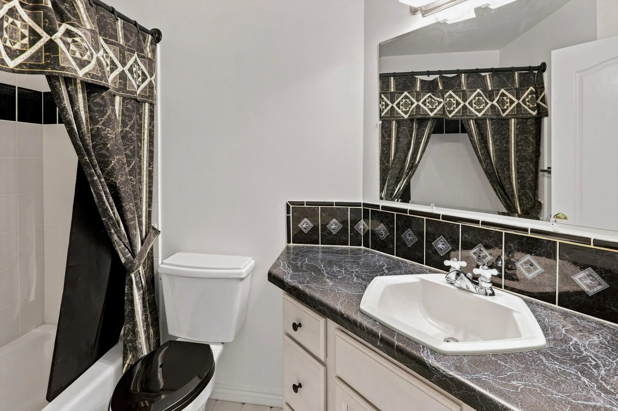 Bathroom featuring an integrated sink with dual faucet, a vanity with cabinet storage, a toilet, and a bathtub with tile surround