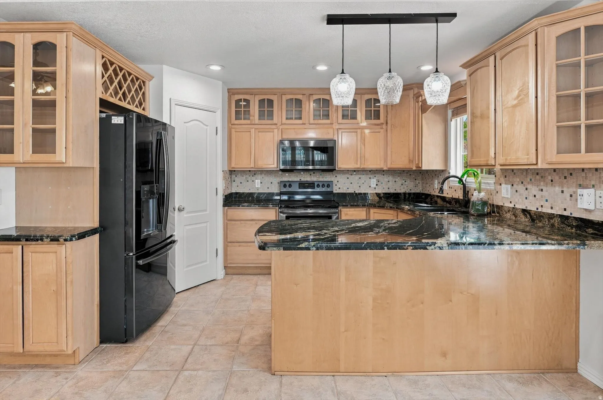 Kitchen featuring light wood cabinetry, dark stone countertops, tile flooring, and a mosaic tile backsplash