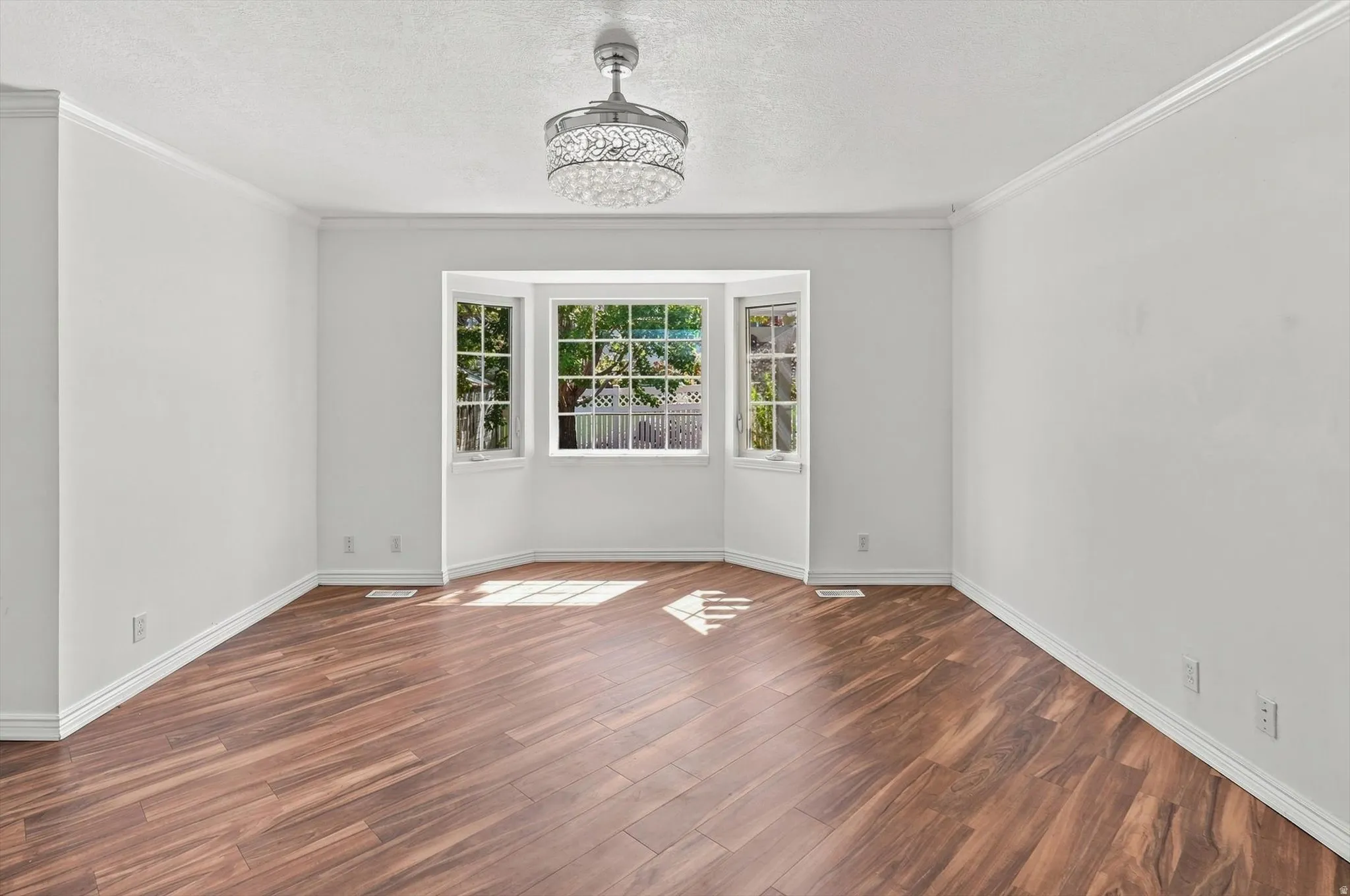 Wood-finish flooring, bay window, decorative ceiling fan, crown molding, and white trim