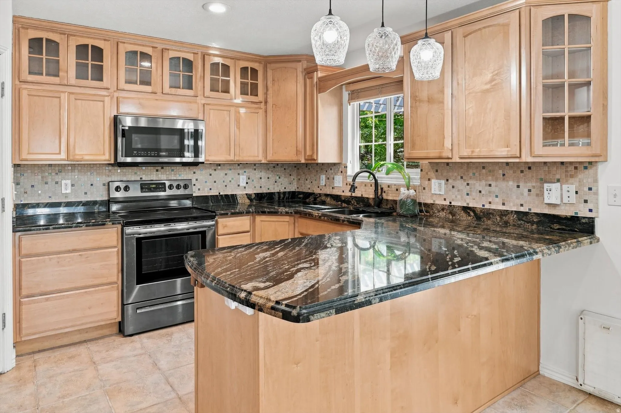 Kitchen featuring light wood-finish cabinetry, stainless steel appliances, dark stone countertops, and a patterned tile backsplash