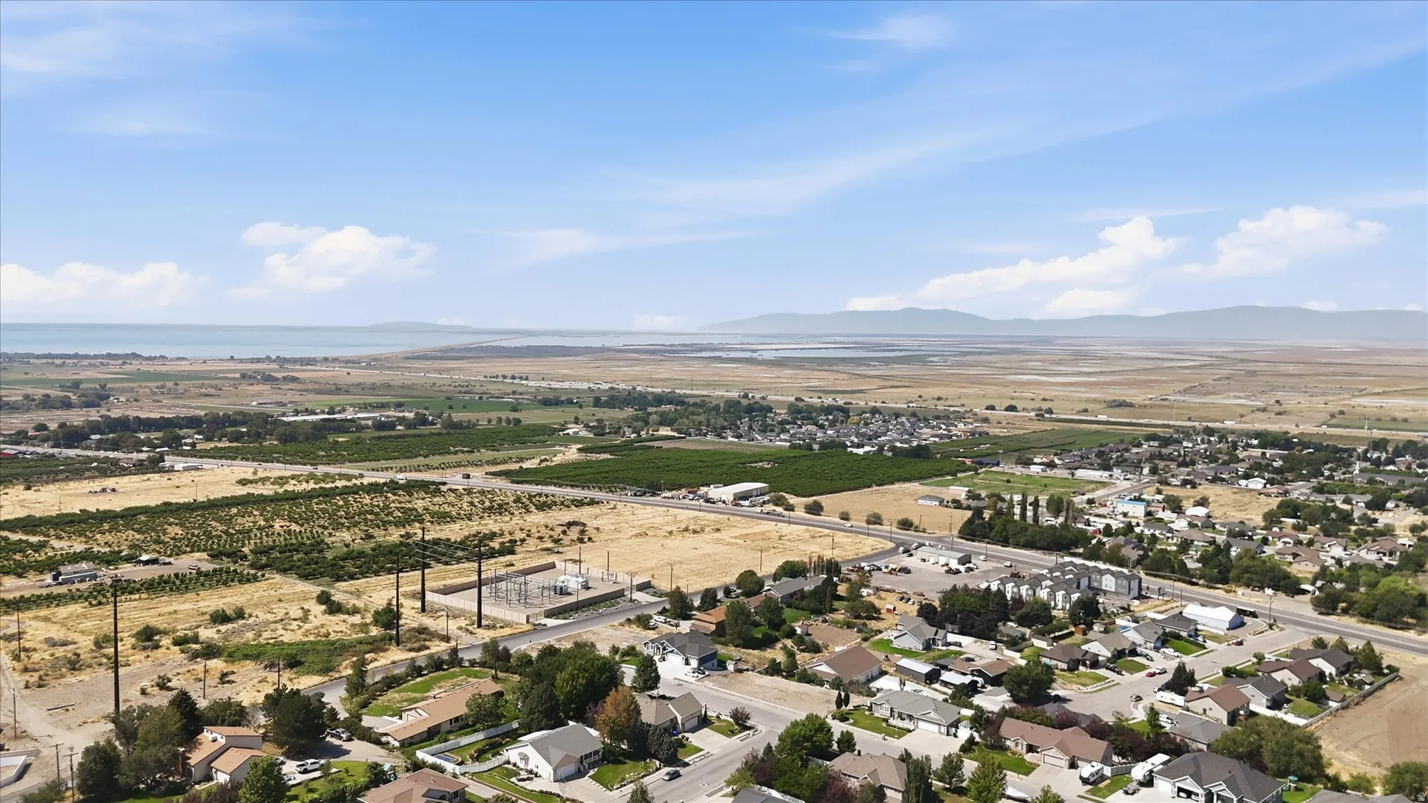 Expansive aerial perspective showcasing a residential area, agricultural land, and a body of water in the distance