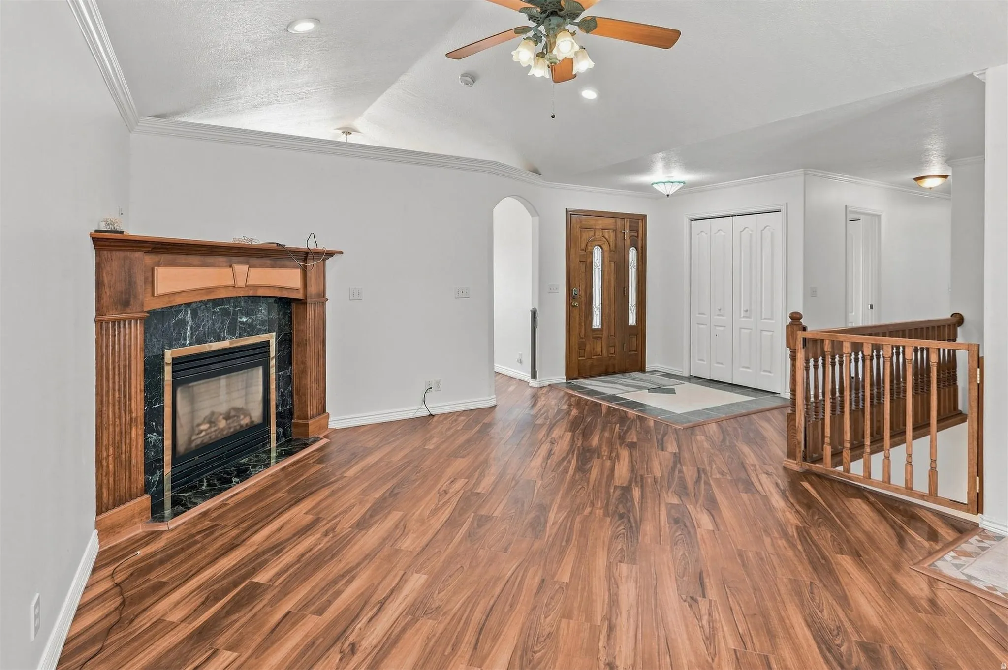 Wood-finish flooring, a fireplace with a wood mantle and dark stone surround, a wood paneled front door, and a wood banister