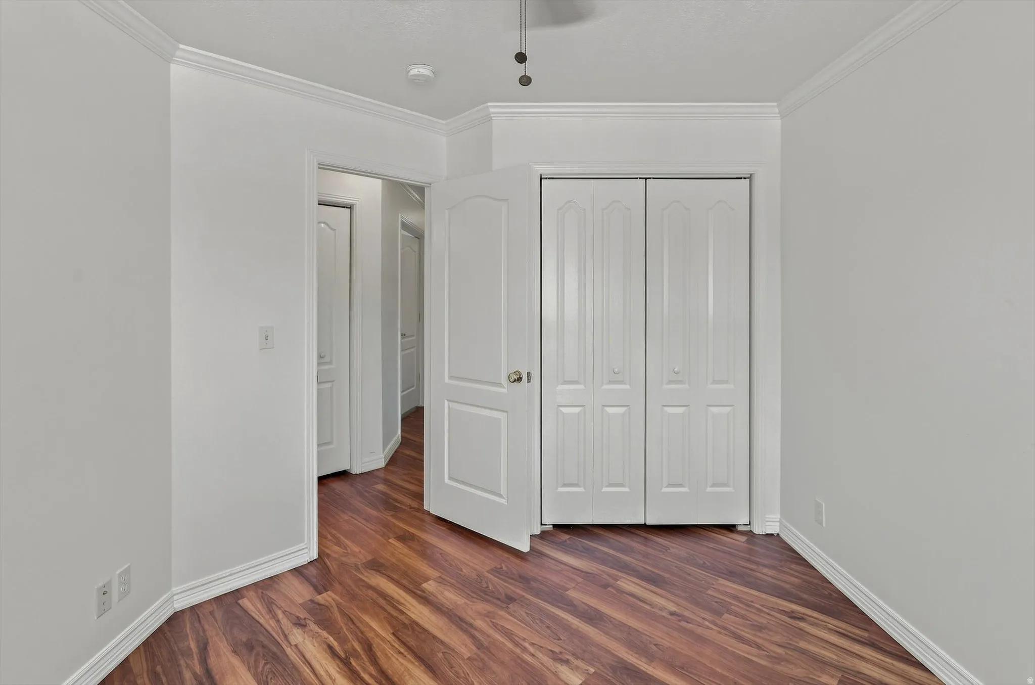 Wood-finish flooring, white walls, white bi-fold closet doors, and white trim