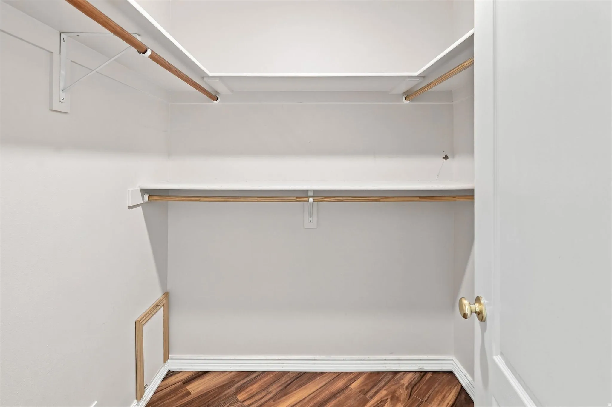 Walk-in closet featuring wood-finish flooring, white walls, and built-in shelving with hanging rods
