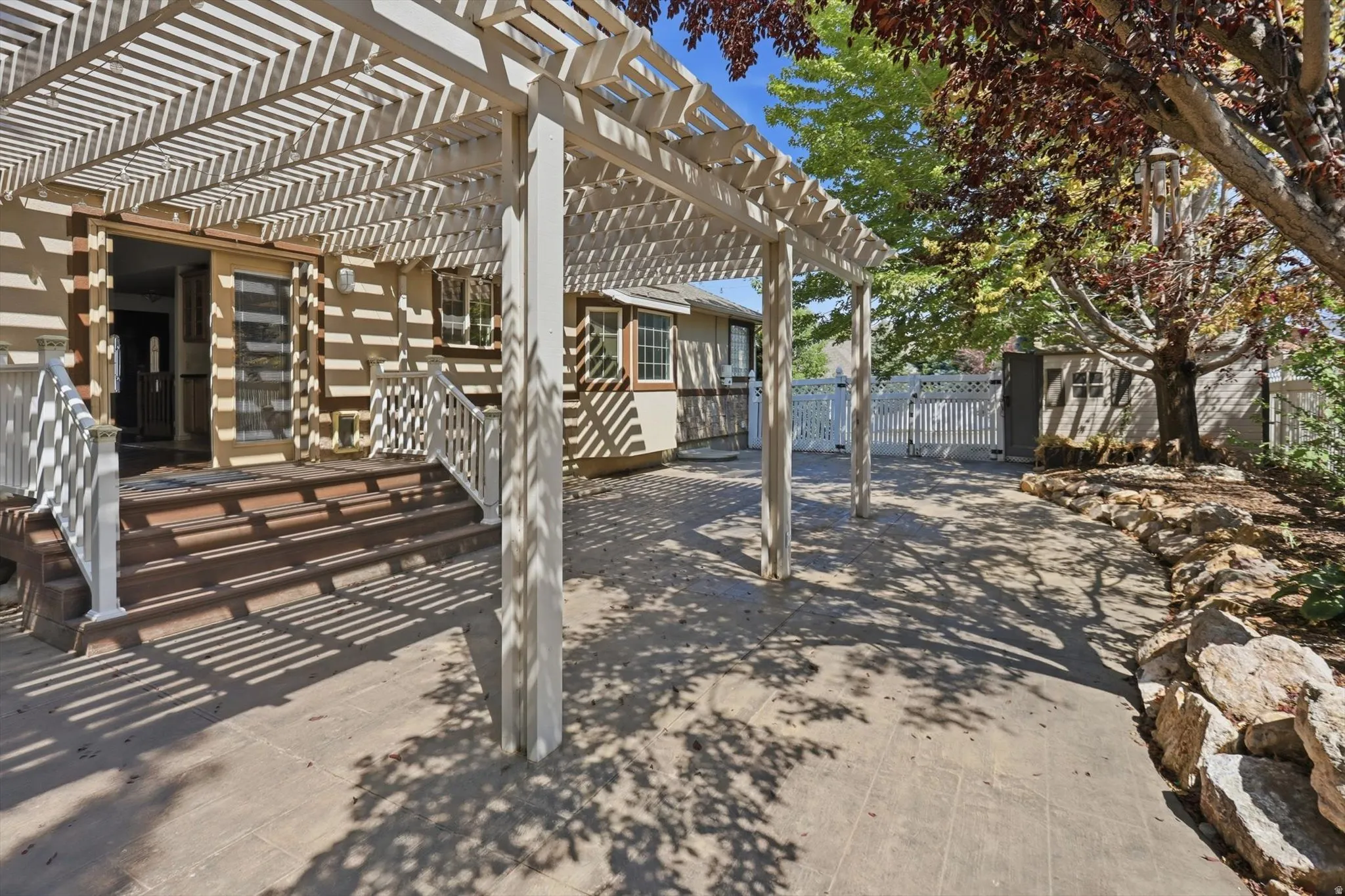 Concrete patio with an overhead pergola, wood deck, white railing, and exterior sliding glass door