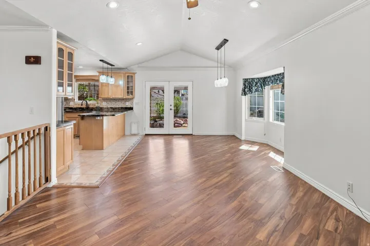 Vaulted ceiling with a ceiling fan, wood-finish flooring, and a bay window