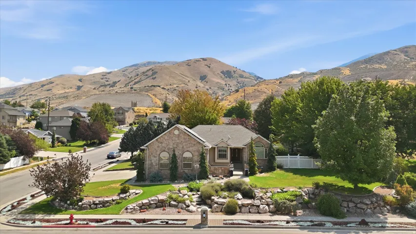 Stone exterior, arched windows, gabled roofline, mature landscaping, and an expansive front yard