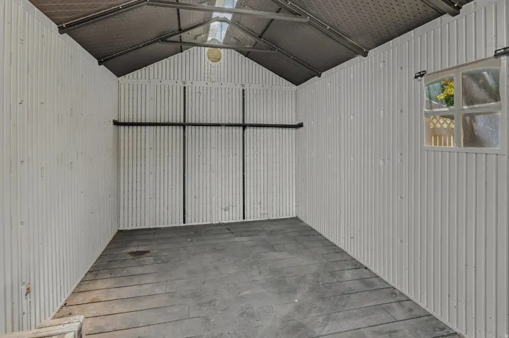 Corrugated metal walls, exposed rafter ceiling, wood-finish flooring, and a single window