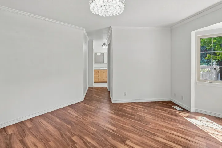 Wood-finish flooring throughout, bright white walls, crown molding, and a multi-pane window