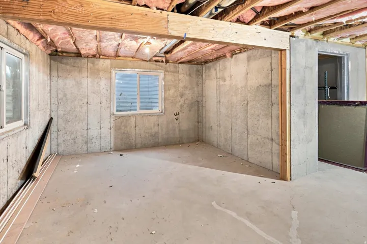 Exposed wood beams, concrete foundation walls, two windows, and concrete flooring