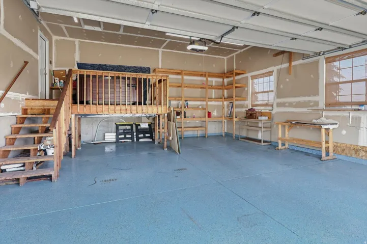 Epoxy-coated flooring, built-in shelving, elevated storage platform, exposed wooden staircase, and multiple windows