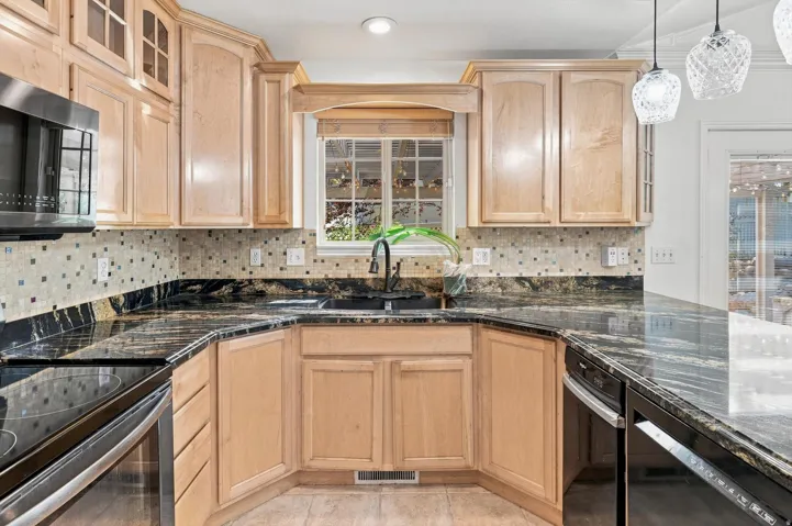 U-shaped kitchen featuring light wood cabinetry, dark polished countertops, mosaic tile backsplash, and stainless steel appliances