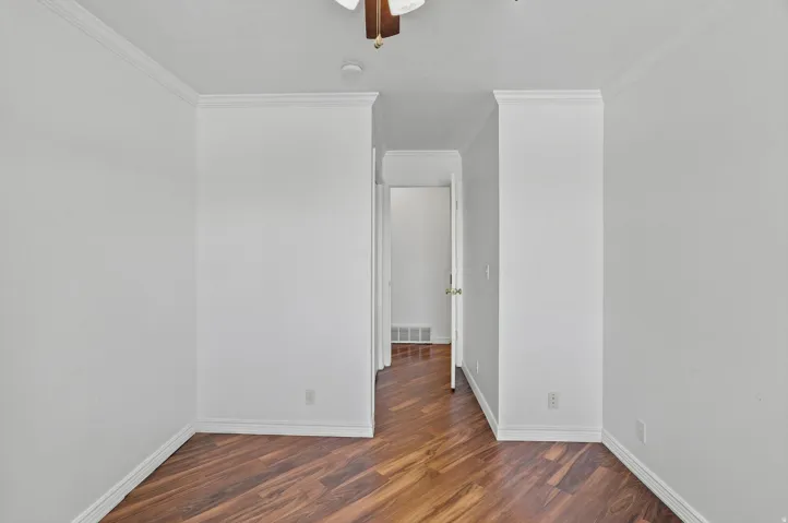 Wood-finish flooring with crown molding and white walls