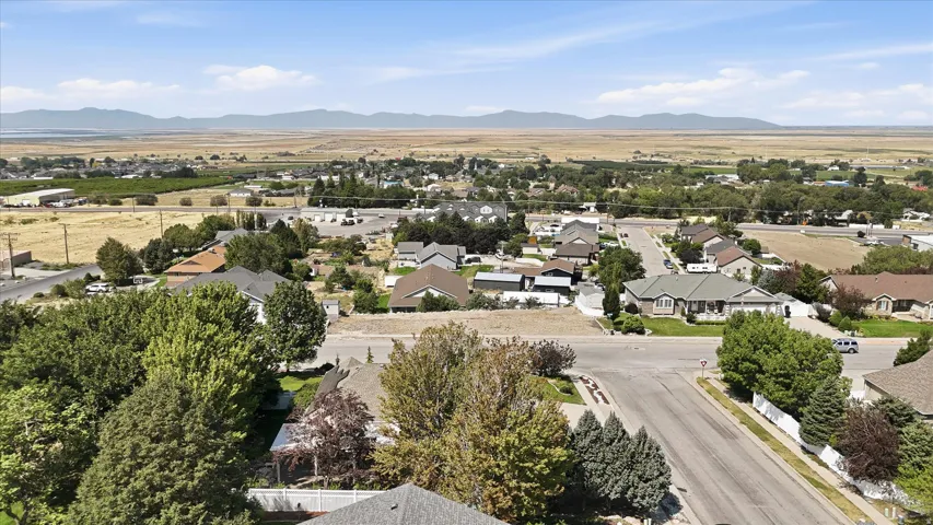 Expansive rural landscape with distant mountains, featuring a residential neighborhood with mature trees and paved streets
