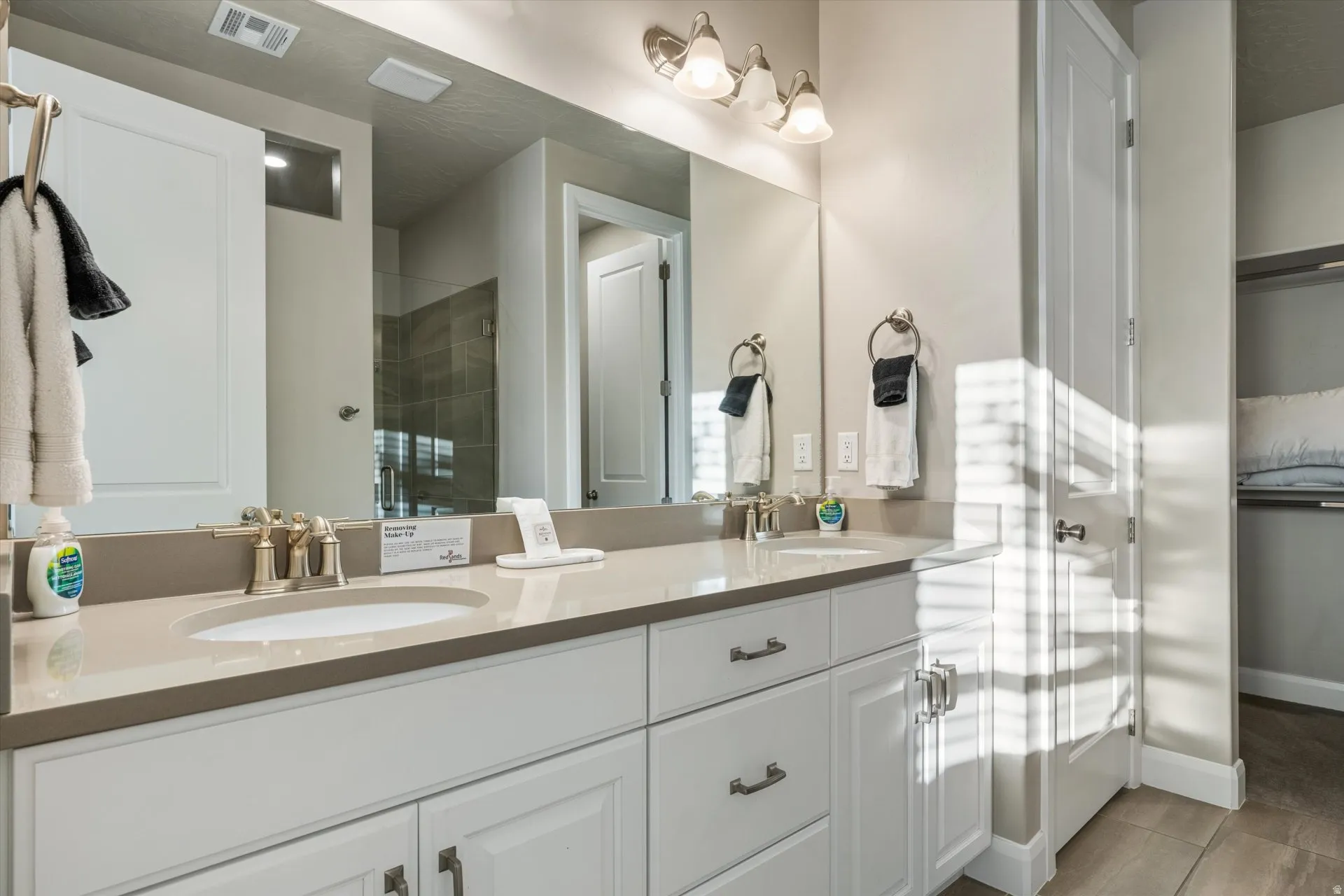 Double vanity with integrated sinks, light-toned countertop, white cabinetry with dark hardware, and brushed nickel fixtures