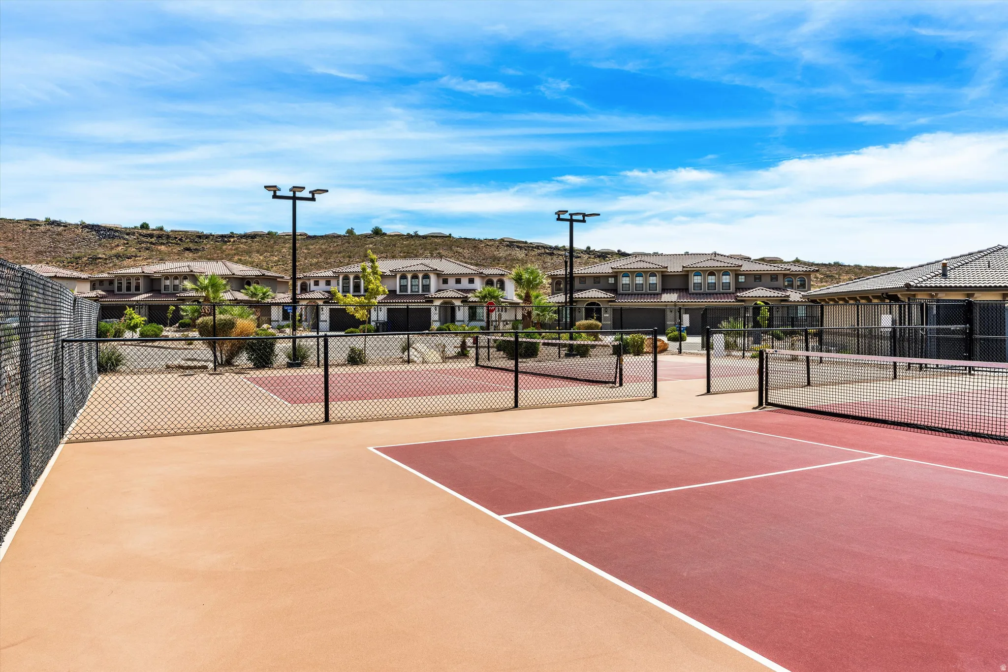 Tennis courts featuring a hard surface, surrounding chain link fencing, and integrated lighting fixtures