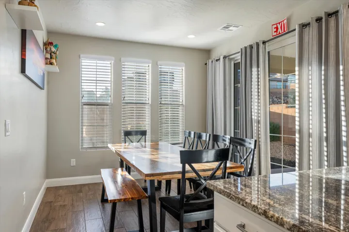 Recessed lighting, wood-finish flooring, sliding glass door, multiple windows with blinds, and a stone-finish countertop