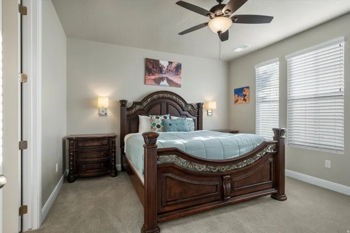 Wall-mounted lighting fixtures, ceiling fan with integrated lighting, two windows with blinds, and carpeted flooring