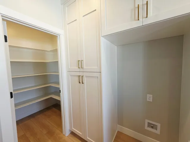 Walk-in pantry with extensive shelving, wood-finish flooring, and white shaker-style cabinetry with gold-tone hardware