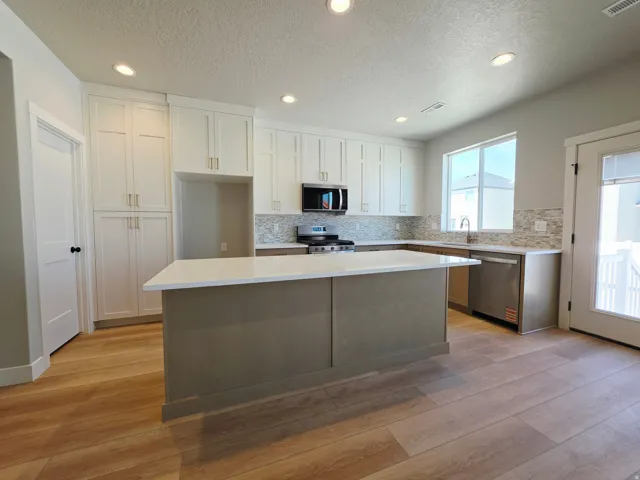 Kitchen featuring wood-finish flooring, recessed lighting, white upper cabinetry, a central island with a light-toned countertop, and a tile backsplash