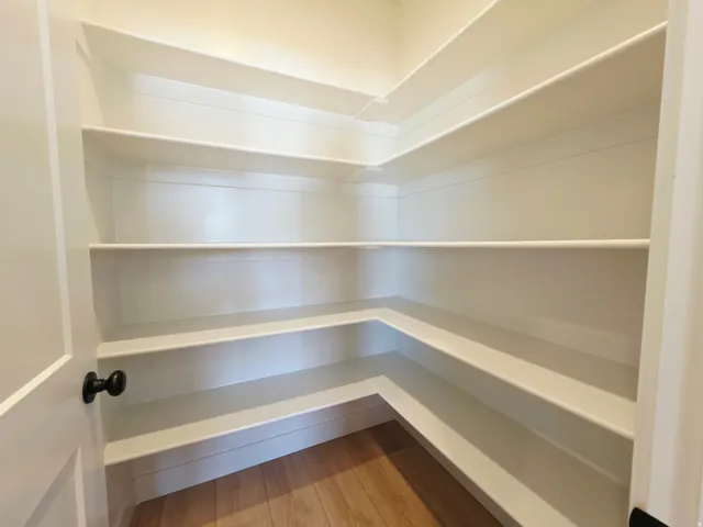 Corner shelving with multiple levels, wood-finish flooring, and a white interior