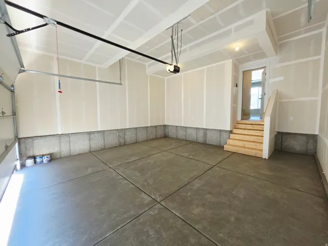 Spacious garage featuring concrete flooring, an automatic garage door opener, and interior access via a wooden staircase
